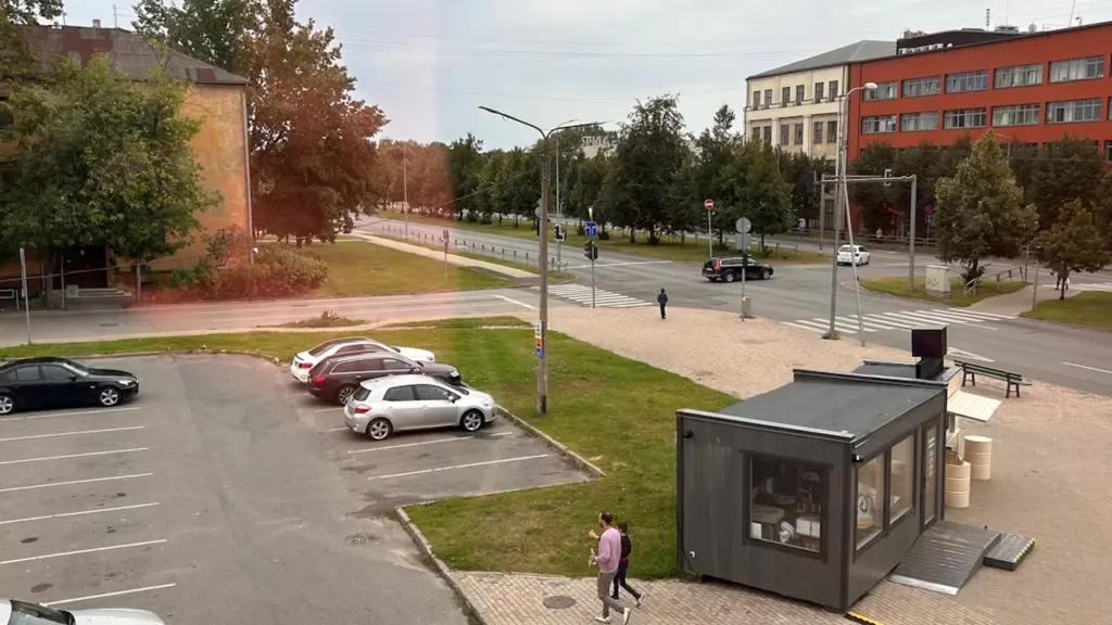 Linnalik vaade autodele ja moodsale väikeehitisele tänaval, mis sümboliseerib nutikat linnakeskkonda ja innovatsiooni.