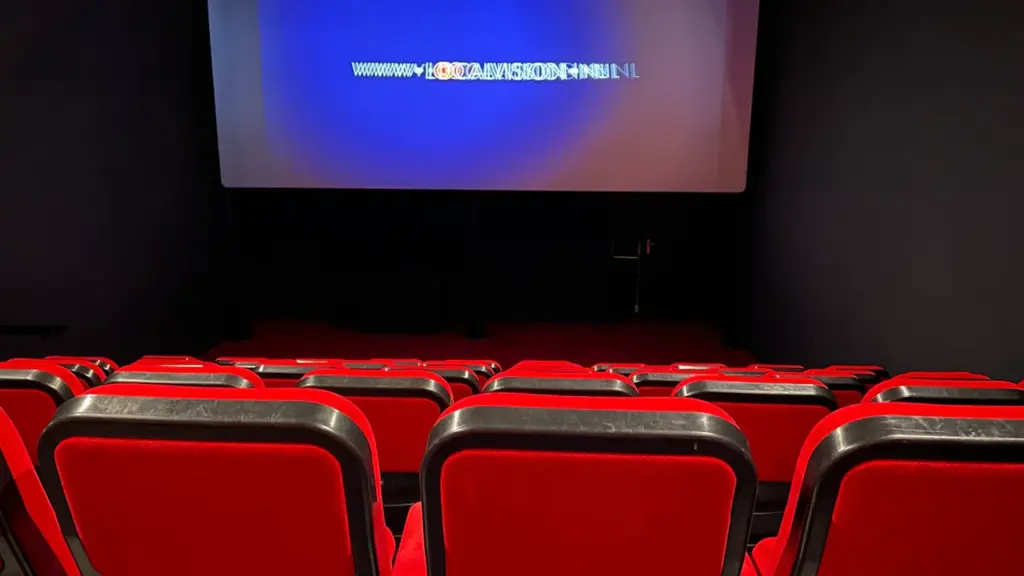 Tühi kinosaal punaste toolide ja suure valgustatud ekraaniga enne filmi algust.