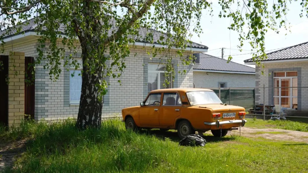 Oranž retroauto pargitud maamaja ees kasepuu all päikeselisel suvepäeval Eestis.