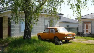 Oranž retroauto pargitud maamaja ees kasepuu all päikeselisel suvepäeval Eestis.